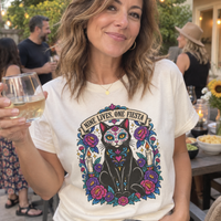 Load image into Gallery viewer, Woman wearing an ivory Nine Lives, One Fiesta Day of the Dead cat graphic tee at an outdoor evening party
