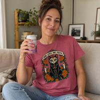 Load image into Gallery viewer, Woman on a sofa wearing a crimson Nine Lives, One Fiesta Day of the Dead cat tee with orange marigolds
