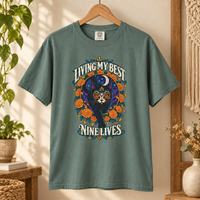 Load image into Gallery viewer, Light Green Living My Best Nine Lives Day of the Dead black cat tee on a wooden hanger
