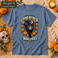 Load image into Gallery viewer, Blue Jean Comfort Colors tee with Living My Best Nine Lives Día de Muertos black cat design and marigolds
