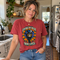 Load image into Gallery viewer, Woman in a kitchen wearing a Chili red Living My Best Nine Lives Day of the Dead cat graphic tee
