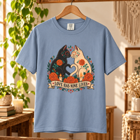 Load image into Gallery viewer, Love Has Nine Lives Day of the Dead black cat t-shirt in Blue Jean on a wooden hanger, Comfort Colors
