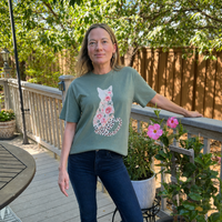 Load image into Gallery viewer, Woman on a garden deck wearing the Bay sage green Wild Rose Cat tee with the rose and leopard print cat design
